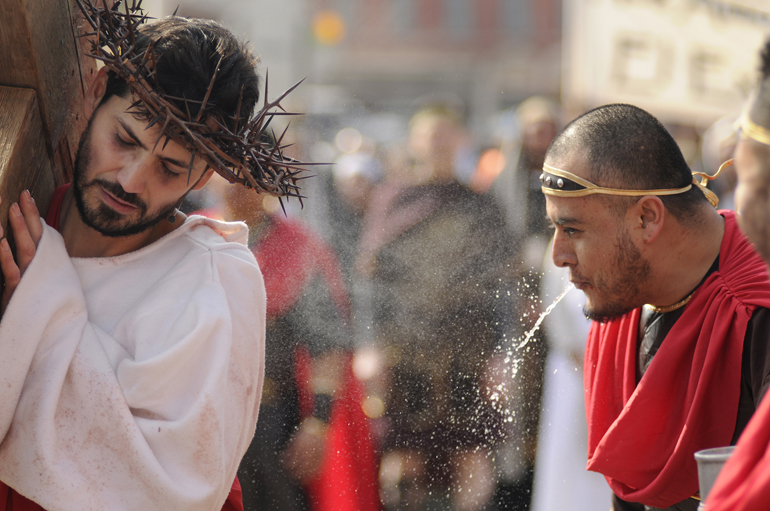 Lorenzo Gutierrez carries a wooden cross as Julio Avila spits water at him during the Living Way of the Cross on Friday, March 29, 2013, outside St. Boniface Catholic Church in Lafayette, Ind. The church\'s annual Living Way of the Cross portrays the fourteen stations of the story of Jesus\' death.