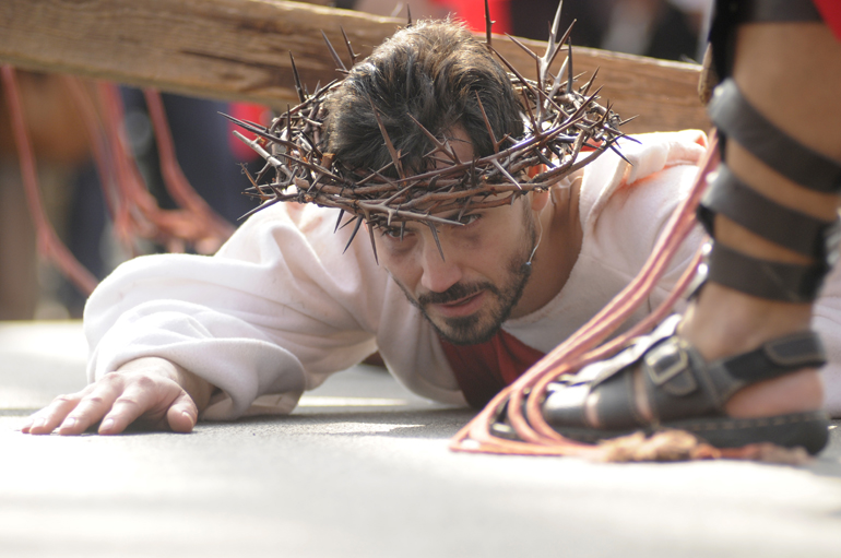 Lorenzo Gutierrez lies on the ground under his cross after falling for a third time during the Living Way of the Cross on Friday, March 29, 2013, outside St. Boniface Catholic Church in Lafayette.