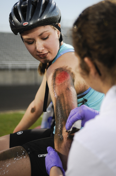 Sophomore Team Revolution rider Christine Ball watches as junior EMT volunteer Jennifer Kempfer cleans her injuries during Little 500 Team Pursuit on Saturday at Bill Armstrong Stadium. Ball received injuries on her leg and shoulder, as well as under her tank top, which her team calls a “fashion top.”