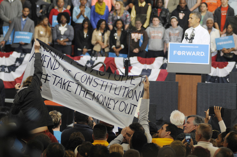 Crowd members hold a banner opposing the abundance of money involved in elections while U.S. President Barack Obama speaks during a presidential campaign stop Sept. 26 at Bowling Green State University's Stroh Center in Bowling Green, Ohio.