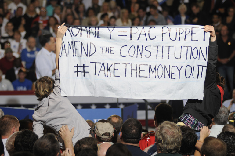 Protesters hold up a sign as former Mass. Governor Mitt Romney speaks during a presidential campaign stop Sept. 26 in Toledo, Ohio.