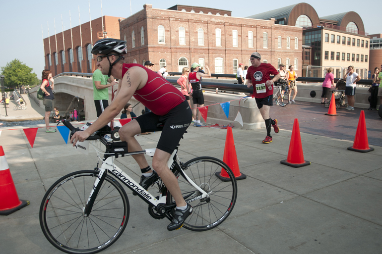 A cyclist and a runner complete the second and third legs of the Tri-Indy Triathlon, Sunday, Aug. 3, 2014. The triathlon route was centered at White River State Park and went as far north as the Major Taylor Velodrome.